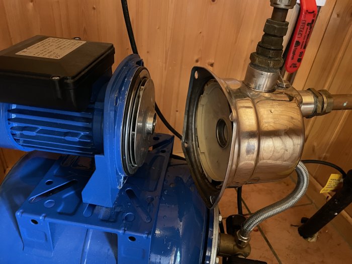 Vattenpump med blå motor och en metallkåpa, synliga packningar och bultar, i ett pumphus.