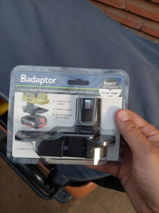 Hand håller en förpackning med en Badaptor, ett batteriadaptertillbehör för att använda Bosch 18V batterier i Ryobi ONE+ verktyg.