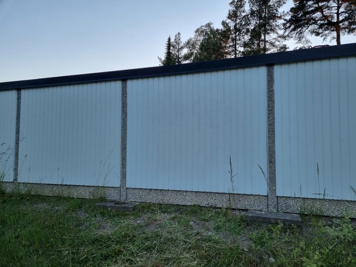 Garagelängor med nymålad vägg där tidigare klotter täckts över, i dagsljus med vegetation i förgrunden.