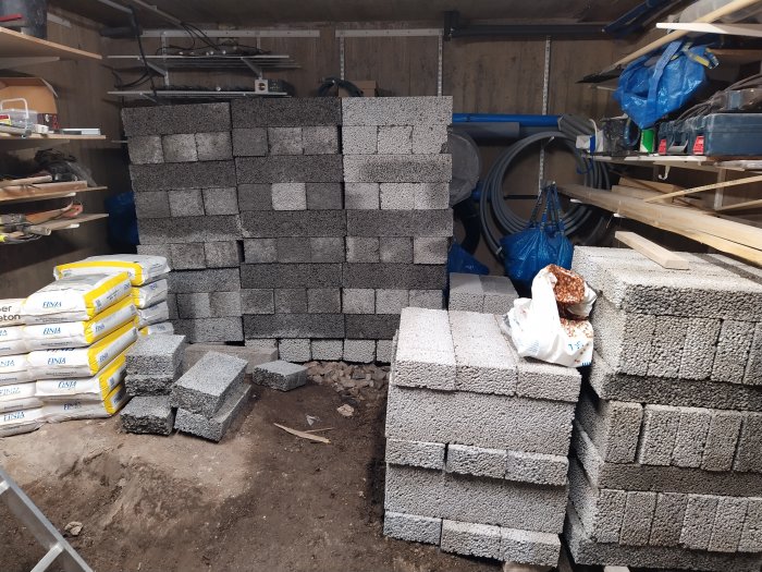 Byggmaterial staplade i källare med betongblock och säckar av cement.