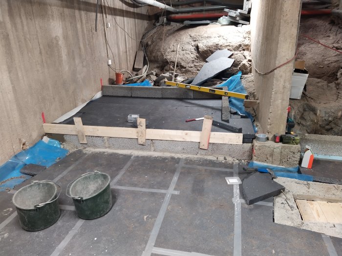 Förberedelse för gjutning med träram och isolering i en källare, verktyg och material spridda omkring.