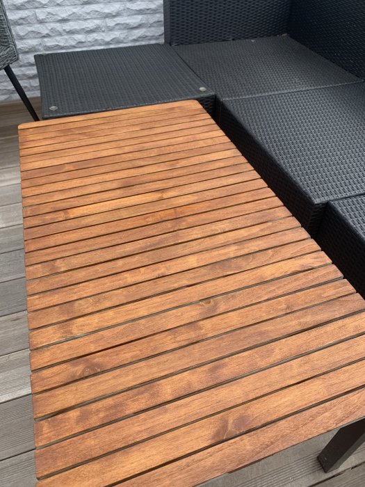 Bord med burmateak på en terrass bredvid svarta rottingmöbler.