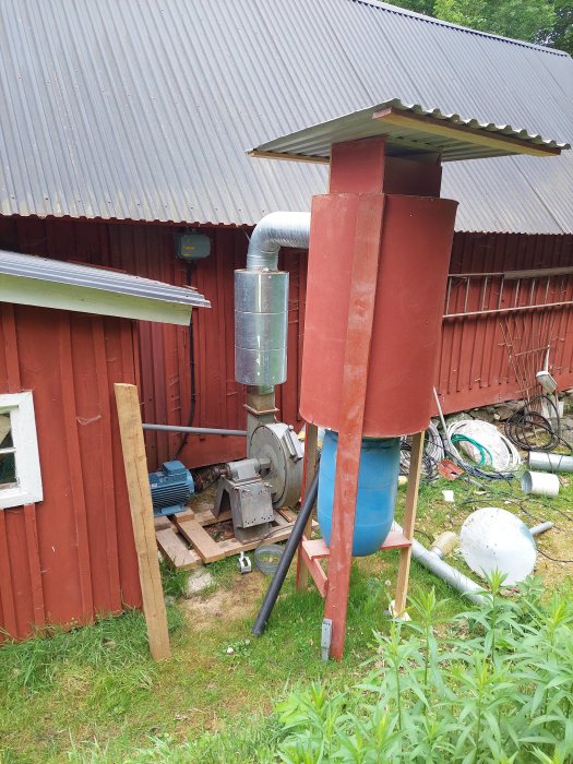 Ventilationssystem med ljuddämpare monterad efter fläkt på röd stuga, mot bakgrund av grönska.