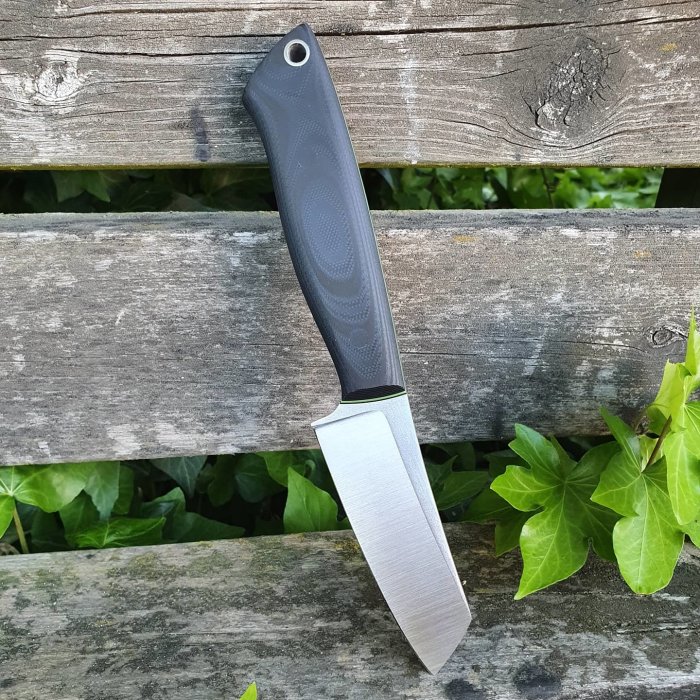 Handgjord kniv med svart Suretouch-skaft och giftgrönt G10-inlägg mot träbakgrund.