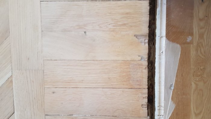 Skadade trägolvslister vid en dörrtröskel som behöver reparation eller utbyte.