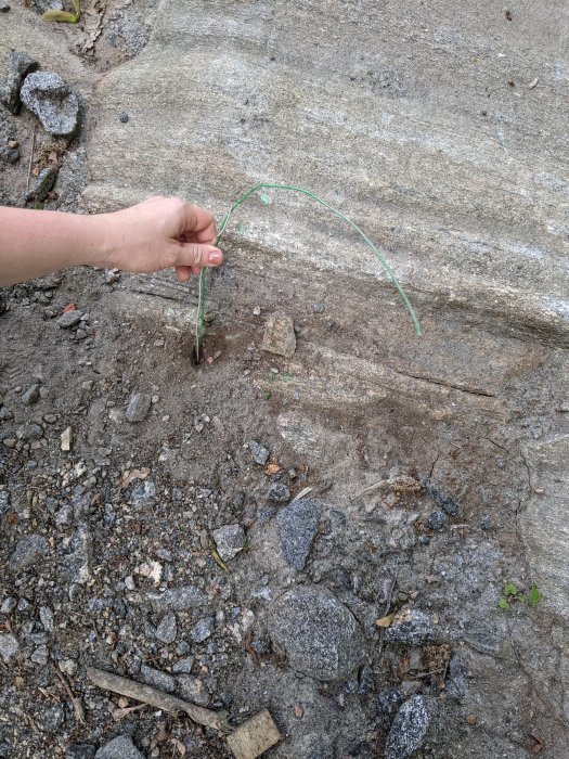 Hand som håller en vitgrön tråd på marken nära insprängt berg vid ett nybygge.