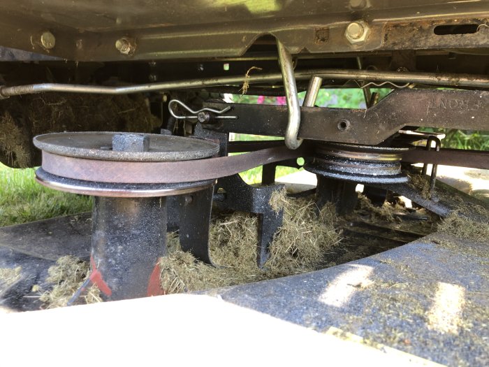 Undersida av gräsklippare som visar skärblad, rem och ackumulerat gräs.