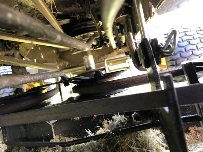 Underrede av trädgårdstraktor med gräsrester och mekaniska komponenter synliga.