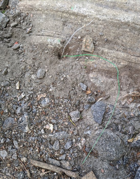 Gröna och vita trådar på marken bredvid insprängt berg och grus.