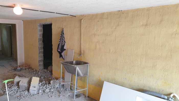 Källarrenovering med nyligen skapat hål i en gulmålad bärande vägg, omgiven av byggmaterial.