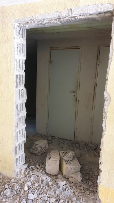 Renoverad källarvägg med nytt öppningshål mitt i bärande vägg, utan synlig uppstöttning, röra av tegelstenar och grus på golvet.