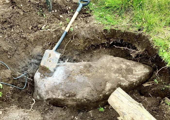 Spade vilar på en stor sten i en grävd grop med jord och gräs runtomkring.