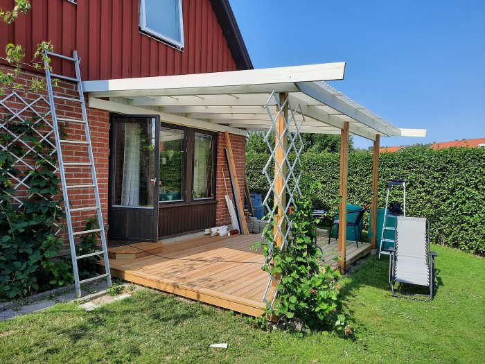 Nyinstallerade vita takfotsbrädor och vindskivor på ett hus med terrass och röd träfasad under en klarblå himmel.