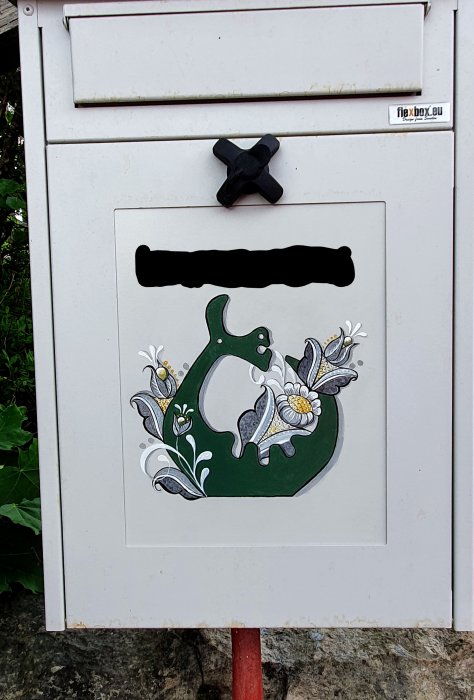 Vit postlåda med dekorativ plåtskulptur av en gecko och blommor på framsidan.