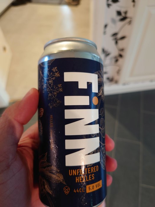 Hand håller en burk öl av märket 'FINN' med texten 'UNFILTERED HELLES', 44 CL, 5,0 VOL.