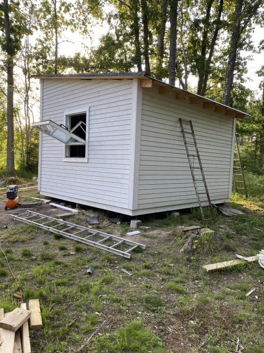 Ett litet hus under konstruktion med nyuppsatta knutbrädor, byggtrappa och verktyg på marken.