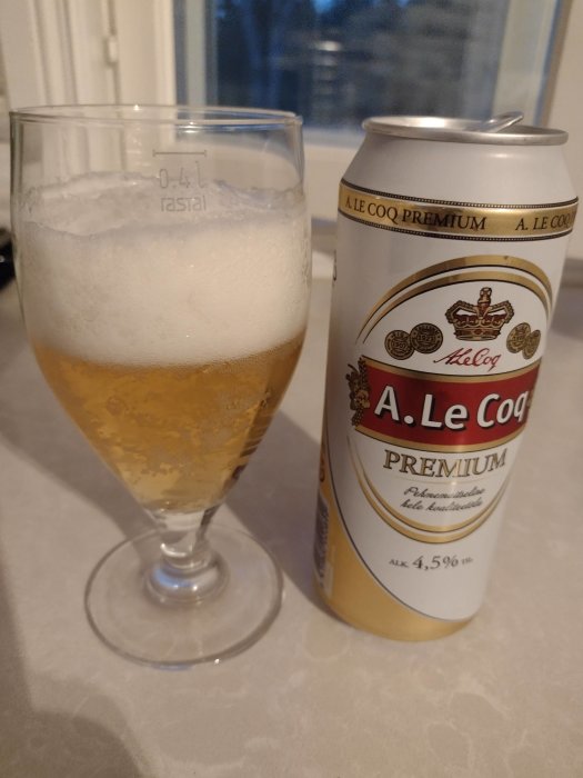 Ett glas med öl och en halvtom estnisk A. Le Coq Premium ölburk på ett bord.