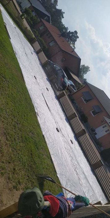 Ny lagd gräsmatta i Skåne täckt med vit presenning för skydd, vattning pågår, soligt väder.