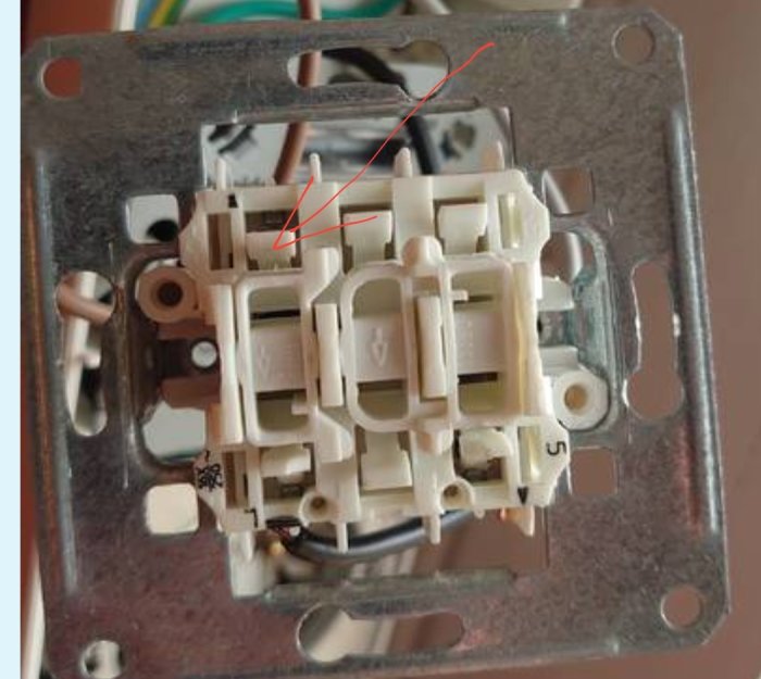 Öppet eluttag med mekanism och röd pil som visar knapp som ska tryckas ned.