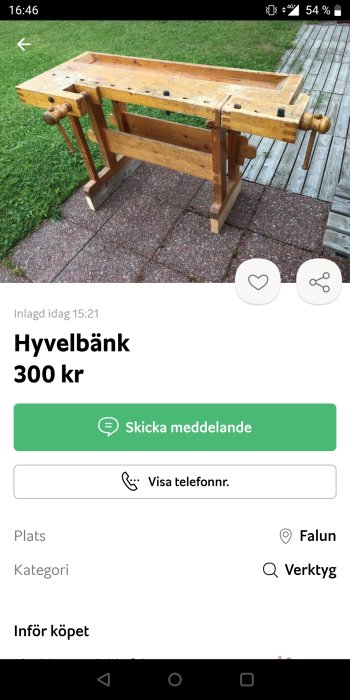 Använd hyvelbänk i trä står på stenlagd uteplats med gräsmatta och trädäck i bakgrunden.