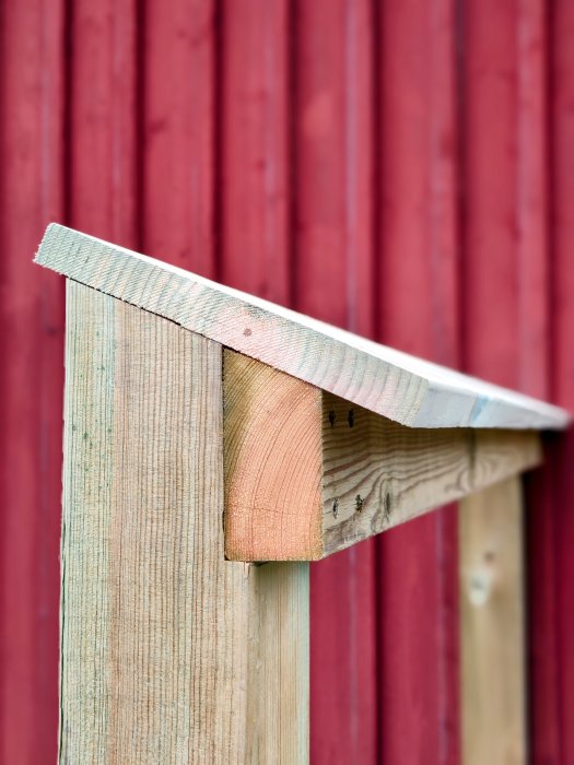 Del av trästomme för ett plank framför en röd trävägg, ommålad och klar för montering.