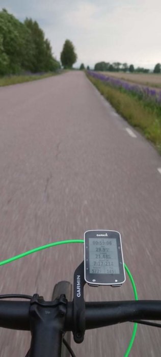 Cyklistens perspektiv med cykeldator på styret och suddig vy av landsväg och blommande fält.