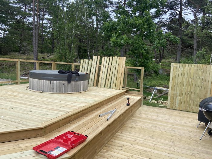 Nybyggd träterrass med badtunna, verktyg på golvet och skog i bakgrunden.
