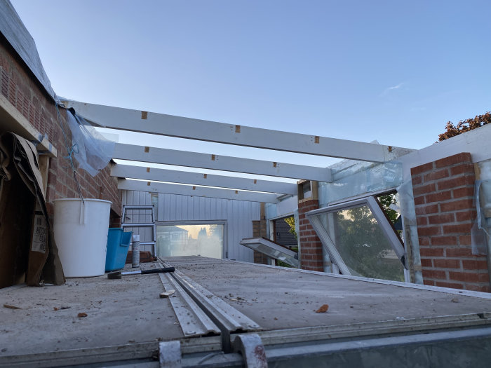 Pågående takrenovering med vita reglar och täckplast mot en tidig morgonhimmel.