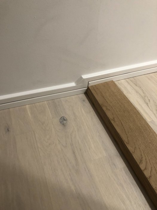 Montering av golvlist i hörn mot ljus vägg och laminatgolv.
