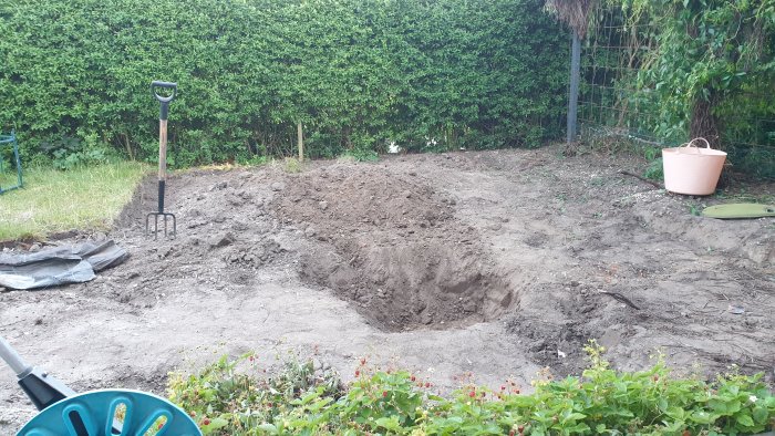 Uppgrävd trädgård förberedd för altanbygge med synlig häck och grävgrejer.