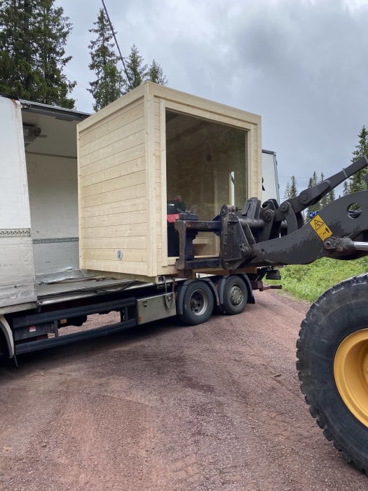 En nybyggd bastu som levereras på ett lastbilsflak med skog i bakgrunden.