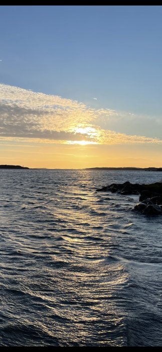 Solnedgång vid havet med skimrande vatten och molnstrimmor på himlen.