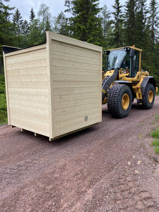 Bakre delen av en timmerkoja med en gul hjullastare till höger på en grusväg.