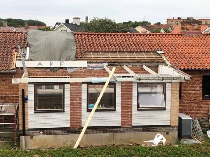 Hus under renovering med täckt tak, byggställning och presenning vikt över en takbalk.