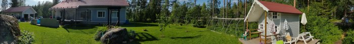 Panoramabild av en gård med nyklippt gräs och gamla tegelstenar som hindrar, hus och lekstuga syns.