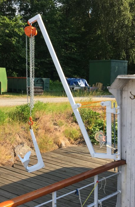 Nymålat ankare i vitt med orange led och slityta hängande från en kran på en brygga.