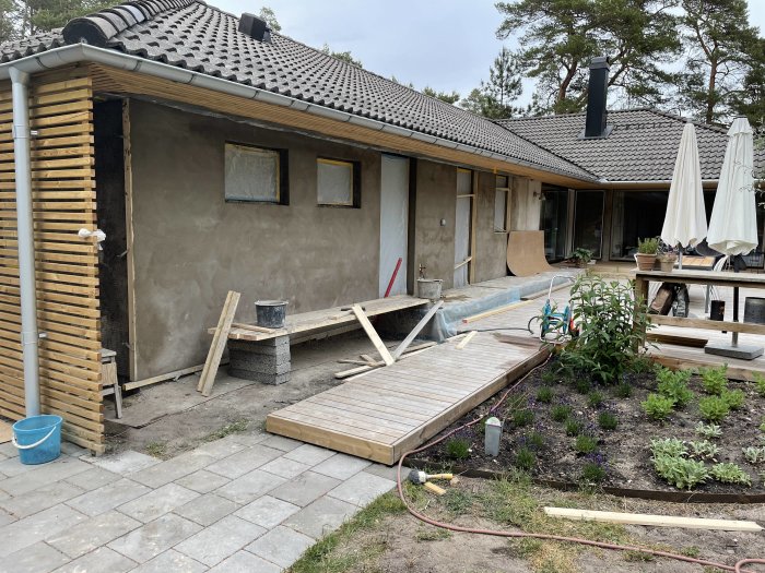 Hus under renovering med nya fönster och nyligen påförd puts på fasaden, byggmaterial på marken.