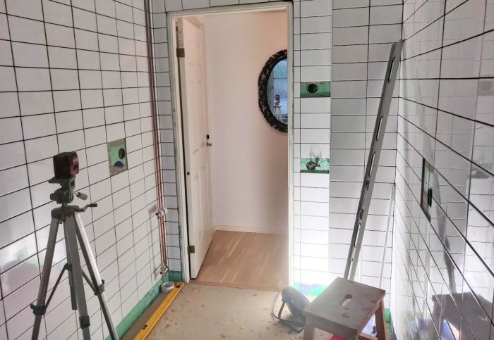 Badrum under renovering med kaklade väggar, byggverktyg och outfogade kakelfogar.