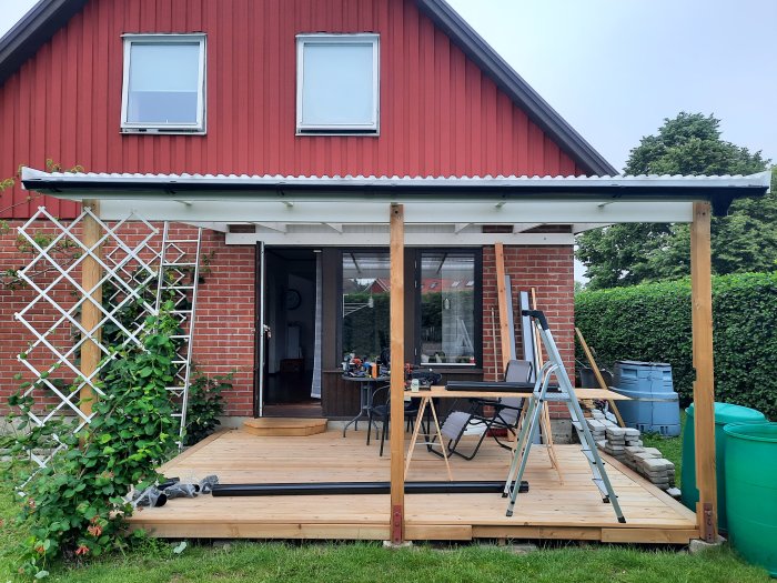 Nyinstallerad hängränna på en terrass med tillfälligt stuprör framför rött hus.