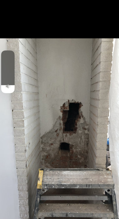 U-formad nisch med öppen spis under renovering och 65 cm mellan vitmålade väggarna, sedd ovanifrån en stege.