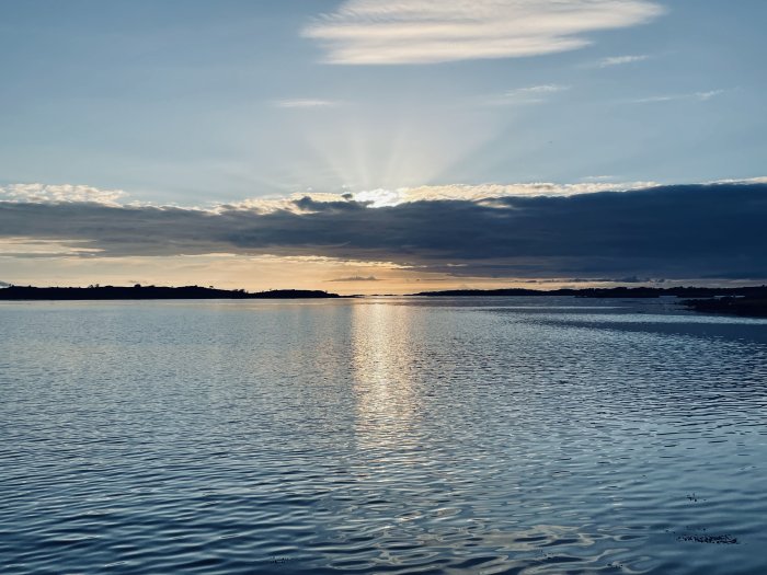 Solnedgång över havet med dramatiska moln och ljusstrålar som reflekterar i vattnet.