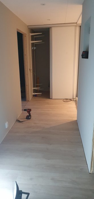 Nyinstallerat ljust laminatgolv i en korridor med verktyg och en garderobsdörr i bakgrunden.