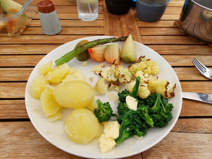 Tallrik med hemodlade grönsaker; sparris, betor, potatis och broccoli, plus lite blomkål, serverad på ett träbord.