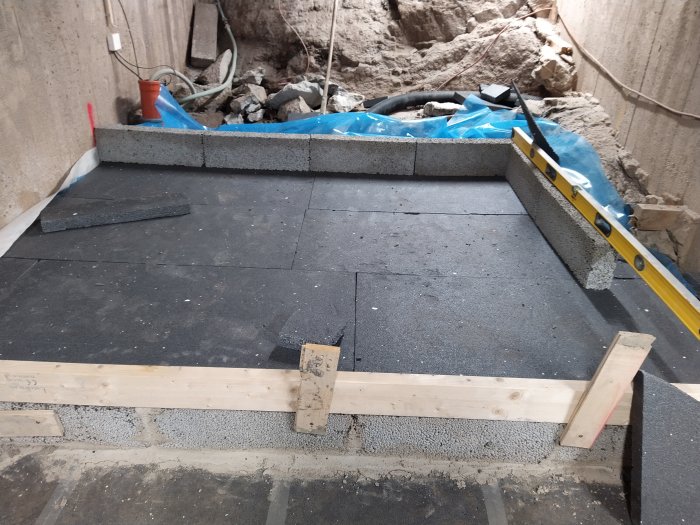 Pågående arbete med isolering och grundläggning, visar isolerplattor och vattenpass på kantsten.
