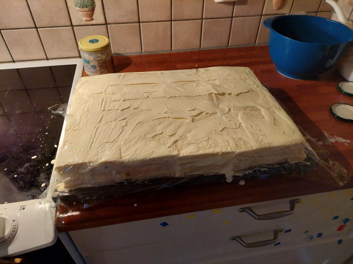 Ett stort smörgåstårta halvfärdigt på ett köksbord, täckt med majonnäs, redo för dekoration.