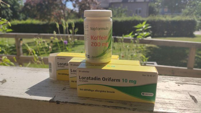 Allergimediciner och koffeintabletter på ett bord utomhus med en trädgård i bakgrunden.