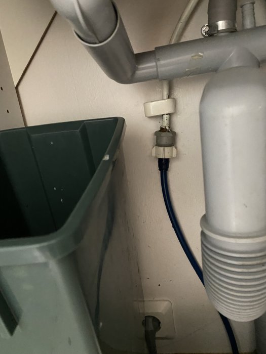 Tilloppsslang ansluten till vattenkran under diskbänk, bredvid grön hink och flexibel avloppsslang.