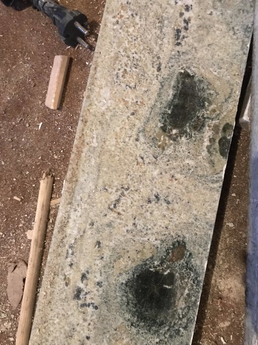En gammal stenfönsterbänk med fläckar och ojämna mönster, möjligen kolmårdsmarmor eller granit, ligger på ett smutsigt golv.