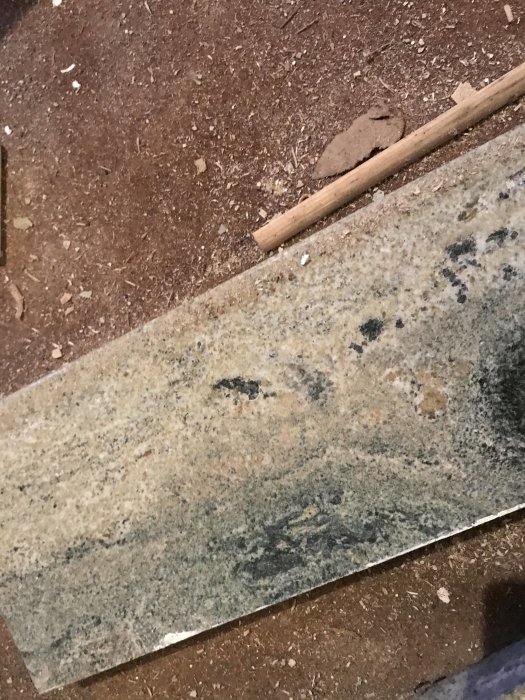 Stenfönsterbänk med grå och svart mönstring, möjlig granit eller marmor, på ett sågspånbeklätt golv.