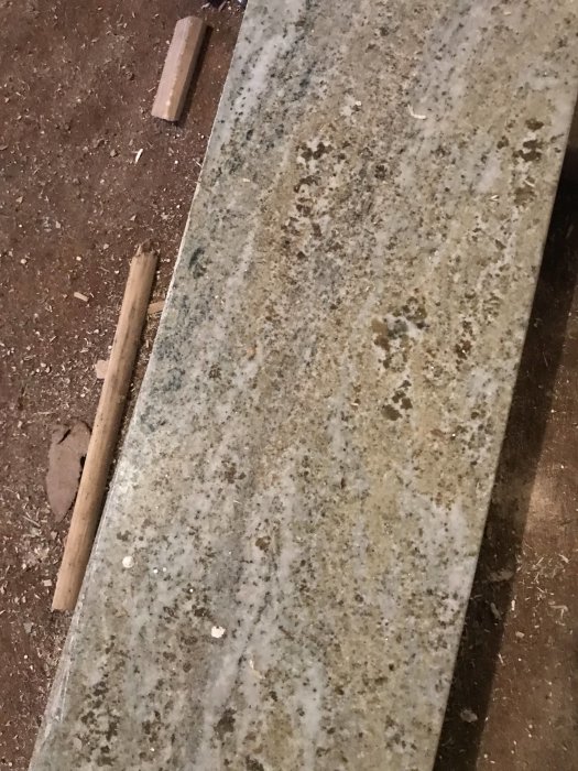 Åldrad stenfönsterbänk med otydliga korn och fläckar på ett dammigt underlag, möjligen marmor eller granit.